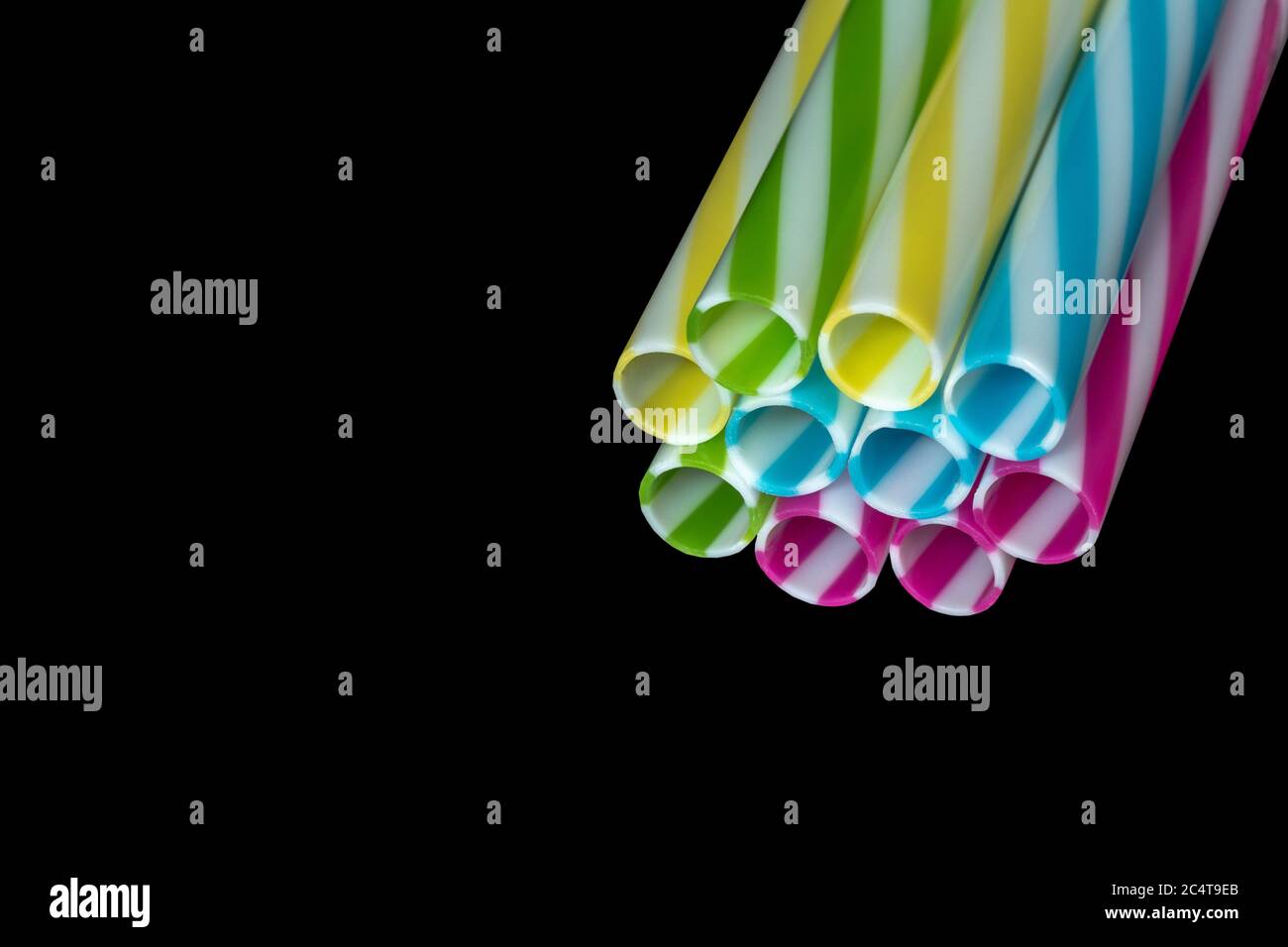 Pile di colorate paglia potabile in plastica a righe, sottoterra nera. Foto Stock