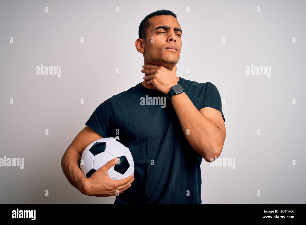 Bell'uomo afro-americano che gioca a piedi tenendo la palla di calcio su sfondo bianco toccando collo doloroso, mal di gola per l'influenza, coodo e infezione Foto Stock