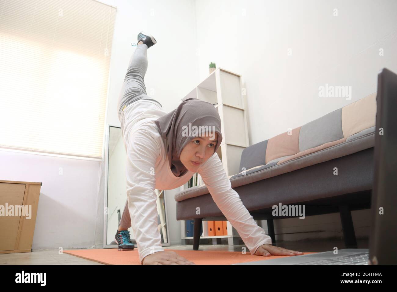 Donna musulmana asiatica che indossa hijab facendo esercizio a casa mentre si guarda video istruzione on-line sul laptop, concetto di allenamento domestico indoor, mantenere sano o Foto Stock