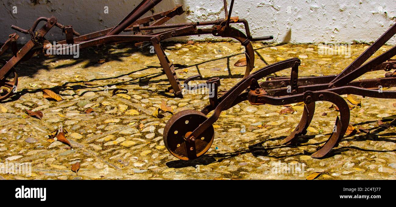 Foto panoramica di vecchi aratri arrugginiti su un terreno di pietra durante luce del giorno Foto Stock
