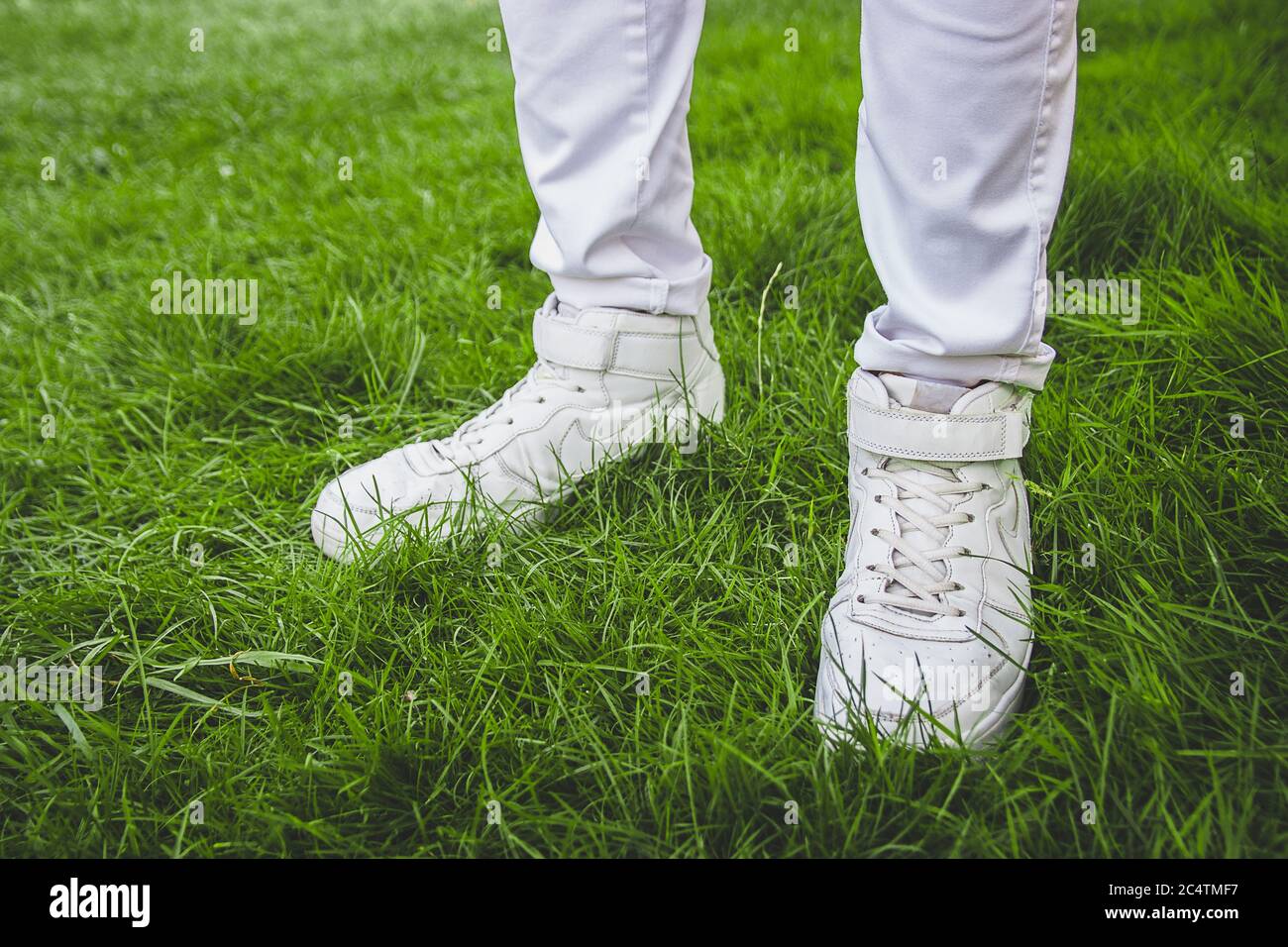 Piedi maschi in scarpe bianche su erba verde. Jeans bianchi. Foto Stock