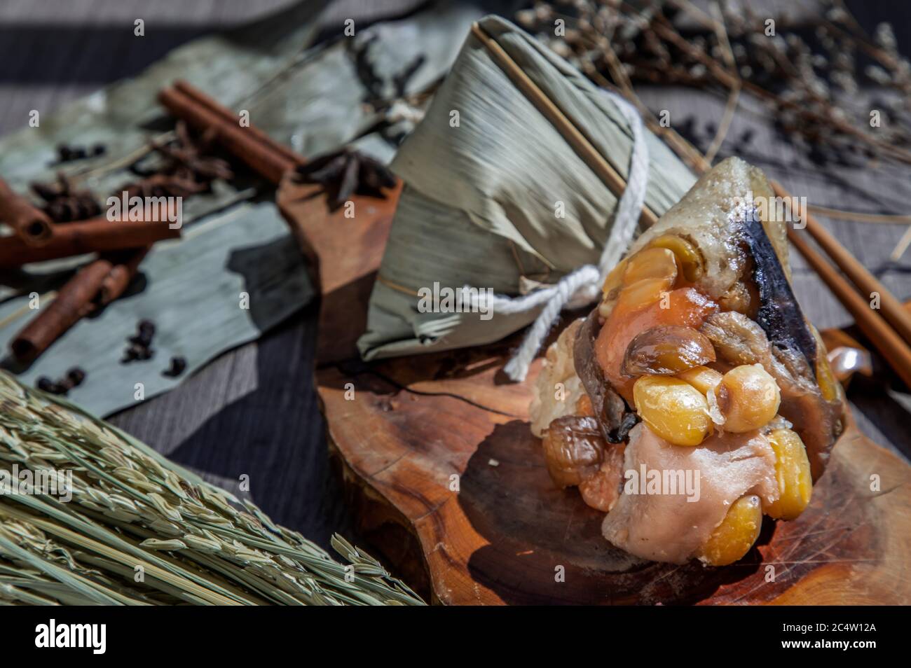 Gnocchi di riso cinese (Zongzi) a forma di piramide avvolto da foglie ingredienti su piastra di legno e bastoncini. Famoso cibo asiatico gustoso fatto a mano in drag Foto Stock