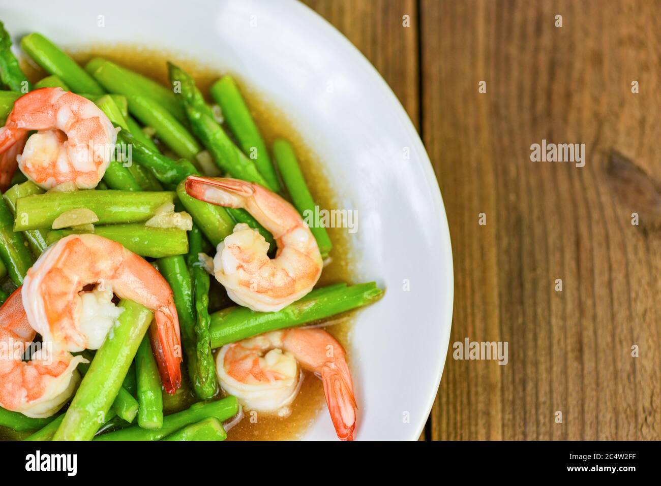 Asparagi gamberi frutti di mare cucinati Salute cibo / Stir gamberetti fritti con asparagi verde su piatto bianco e sfondo tavola di legno Foto Stock