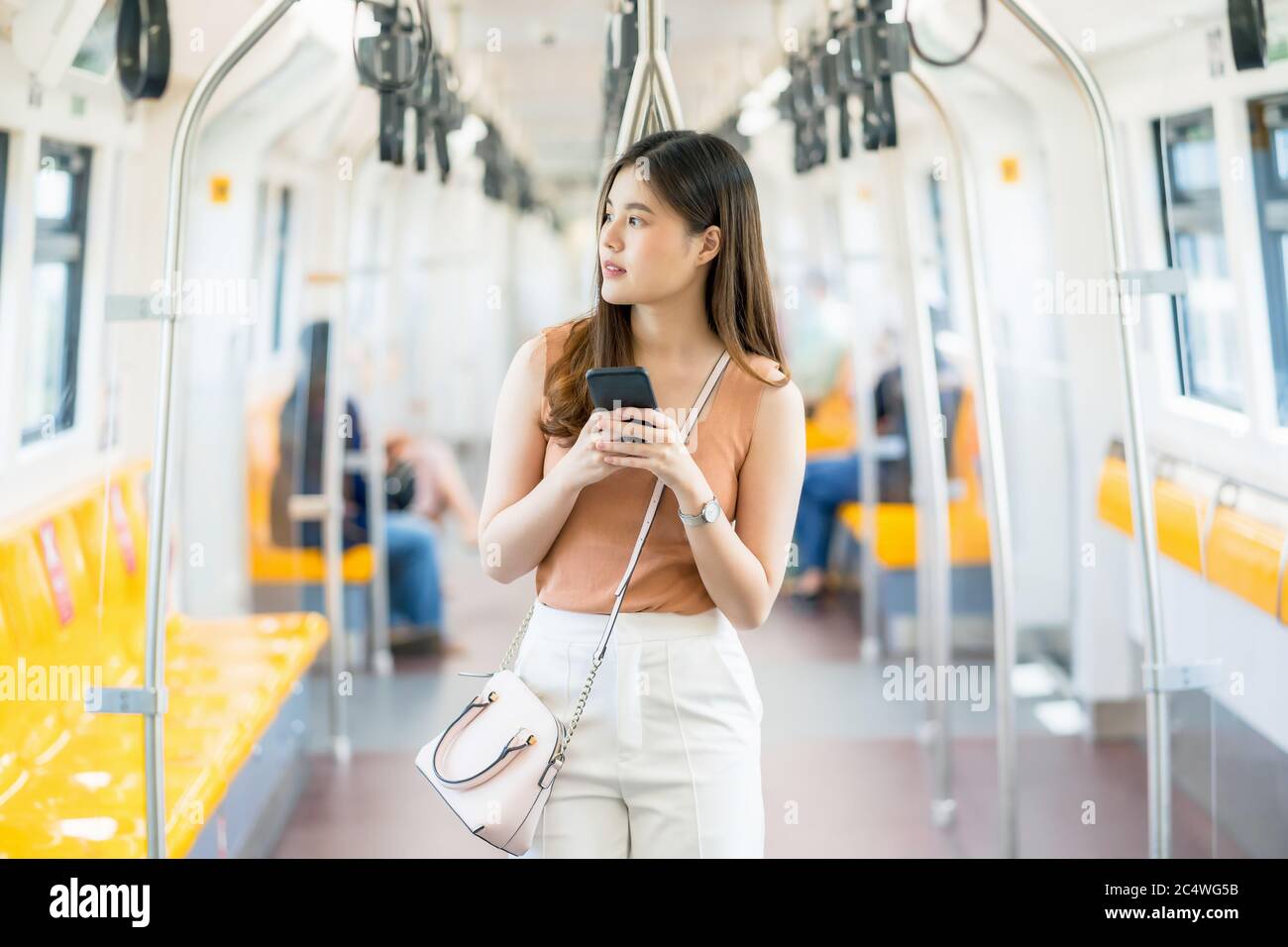 Giovane donna asiatica passeggero utilizzando smartphone e guardando fuori dal treno della metropolitana quando si viaggia in grande città, pendolari e trasporti co Foto Stock