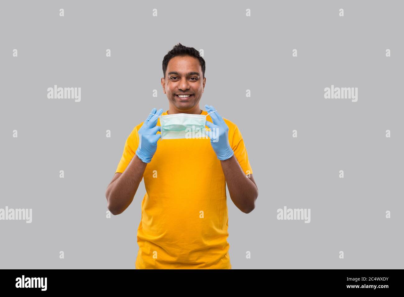 L'uomo indiano mette sulla maschera medica e guanti in camicia gialla isolata Foto Stock