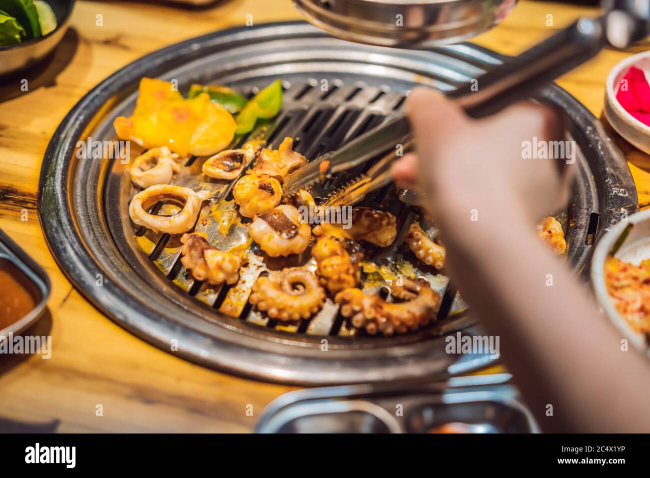 Donna grigliare barbecue su griglia a rete di fuoco di carbone. Cucina coreana o giapponese tradizionale barbecue alla griglia Foto Stock