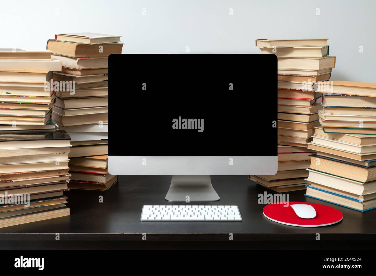 Computer da tavolo circondato da pile di libri sul tavolo. Concetto di studio online e preparazione agli esami. Foto Stock