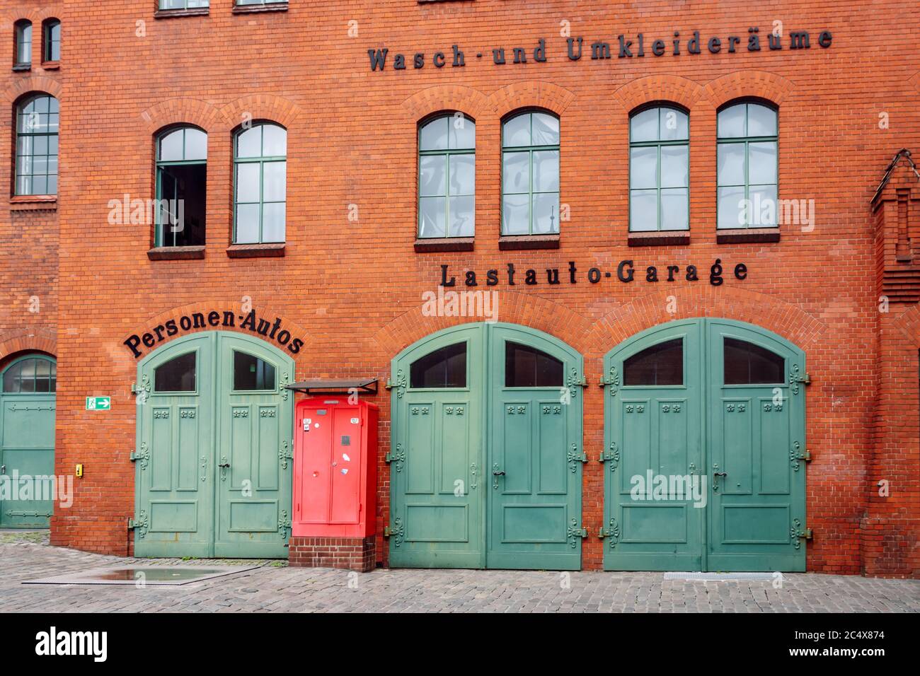 Bella facciata industriale in mattoni rossi con tre porte vintage garage verde. Ex garage camion nel cortile del Cente culturale Kulturbrauerei Foto Stock