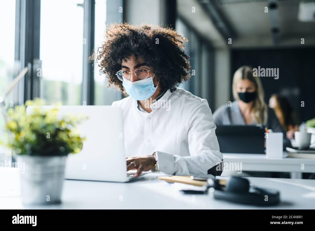 Ritratto di giovane uomo con maschera facciale di nuovo al lavoro in ufficio dopo il blocco. Foto Stock