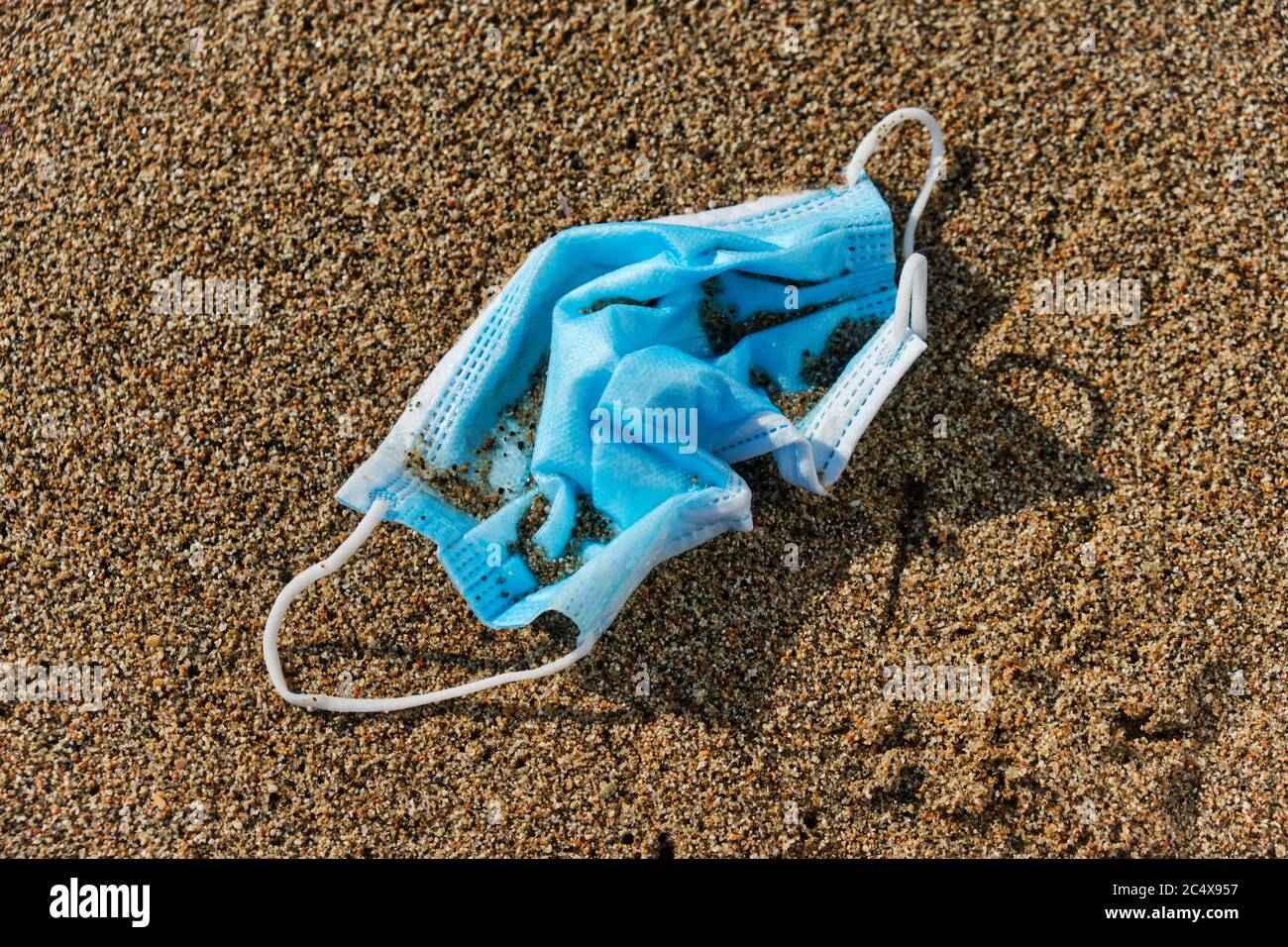 primo piano di una maschera chirurgica blu usata gettata sulla sabbia bagnata della riva di una spiaggia Foto Stock