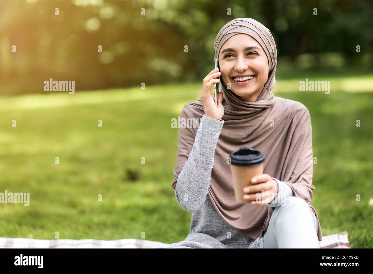 Felice musulmana che parla al telefono e beve caffè Foto Stock