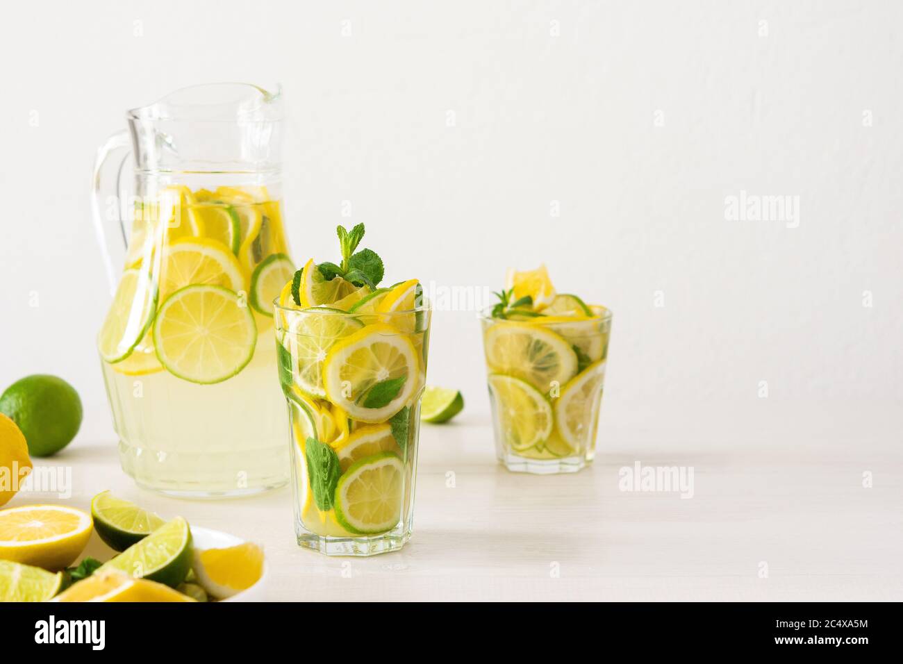 Bevanda estiva rinfrescante di limone, lime e menta, caraffa con limonata e bicchieri e fette di agrumi Foto Stock