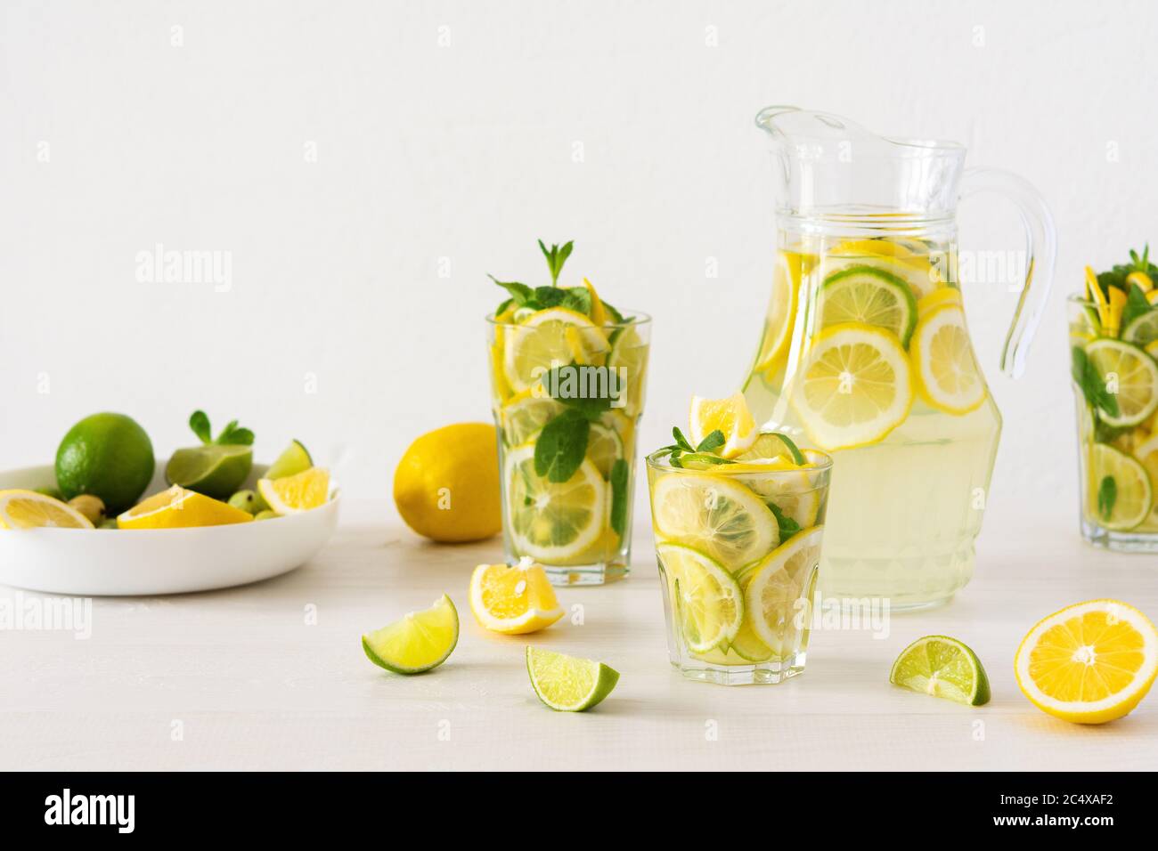 Bevanda estiva rinfrescante di limone, lime e menta, caraffa con limonata e bicchieri e fette di agrumi Foto Stock
