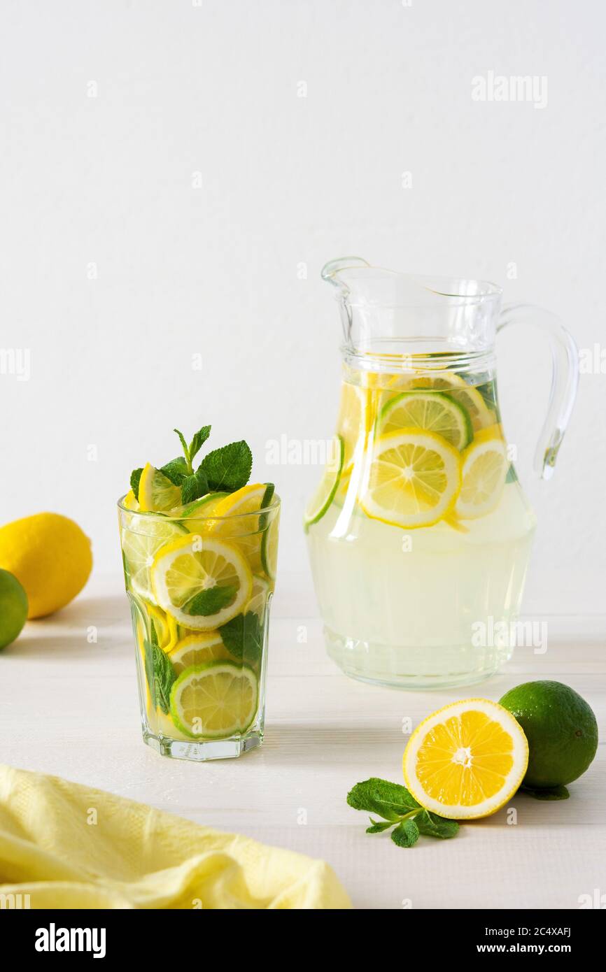 Bevanda estiva rinfrescante di limone, lime e menta, caraffa con limonata e bicchieri e fette di agrumi Foto Stock