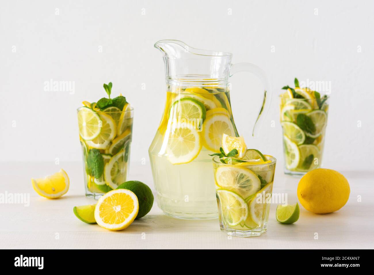 Bevanda estiva rinfrescante di limone, lime e menta, caraffa con limonata e bicchieri e fette di agrumi Foto Stock