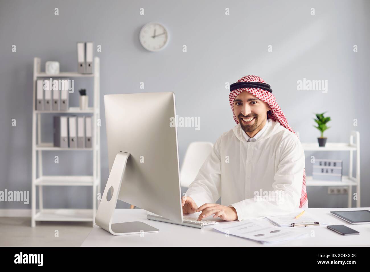 Uomo arabo che lavora analizzando la digitazione a un tavolo con un computer in ufficio. Foto Stock
