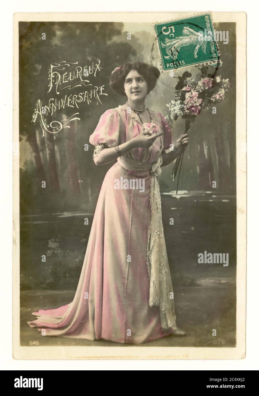 Primi anni '900 francese sentimentale tinta saluti cartolina di una bella donna in un lungo abito estivo che scorre tenendo un bouquet di fiori - il messaggio è 'Happy Anniversary', Francia, circa 1911 Foto Stock