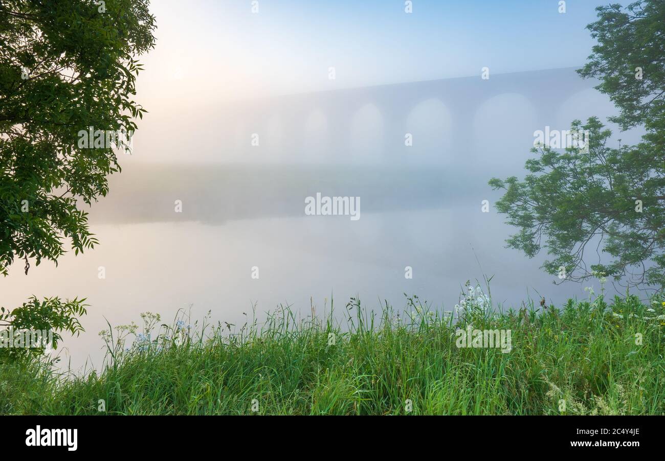 Arthington Viaduct è appena visibile attraverso la nebbia di mattina presto in una mattina di primavera tardi, il fiume Wharfe perfettamente riflettere gli archi ferroviari. Foto Stock
