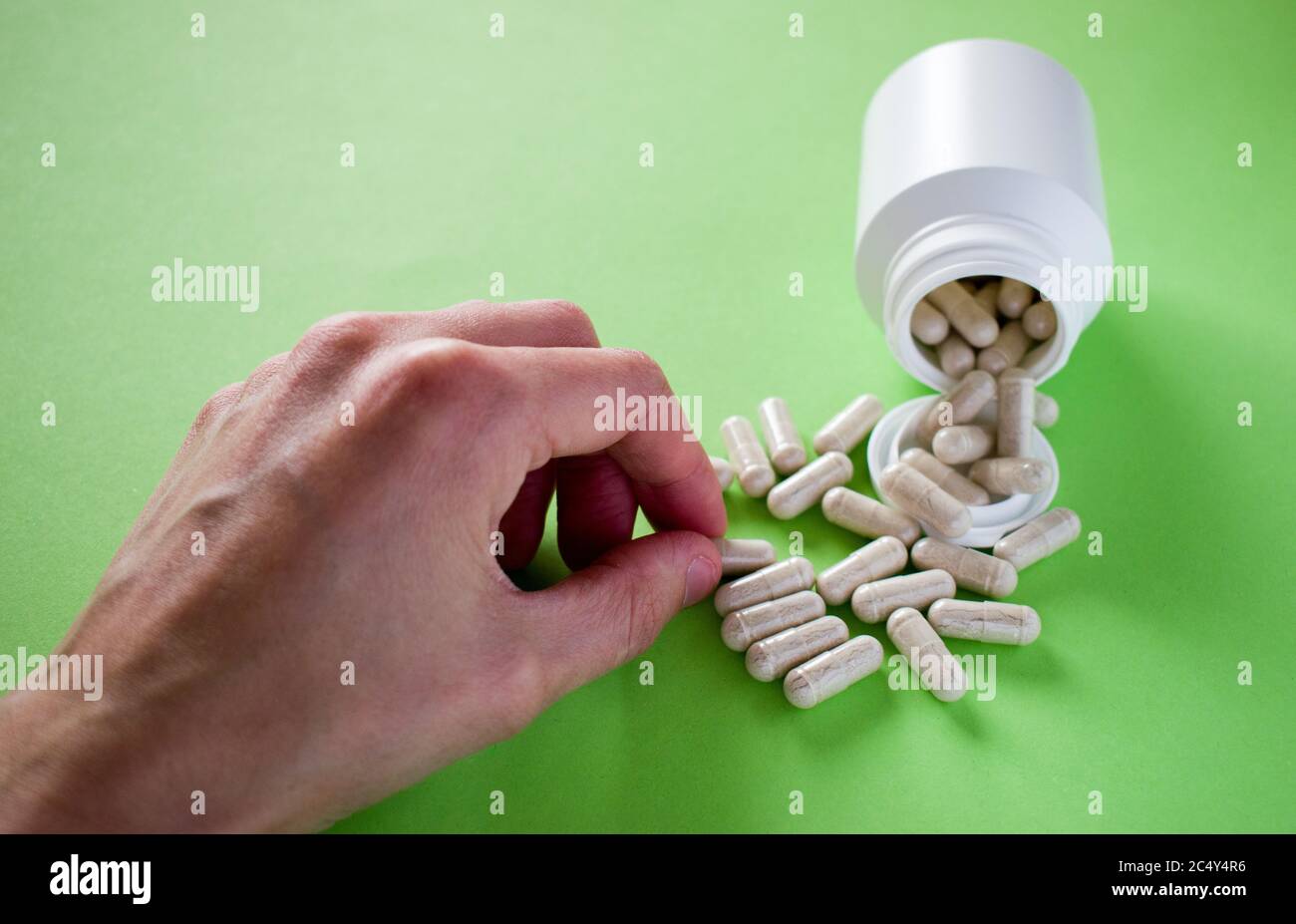 Mano che prende la pillola medica da flacone di pillola versato su sfondo verde Foto Stock