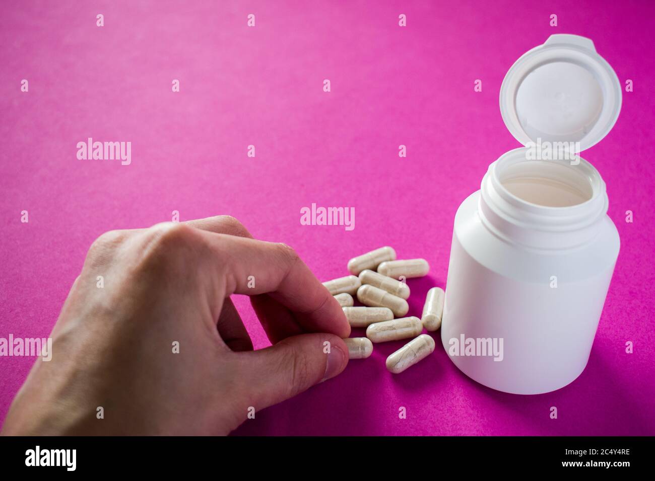 Mano che prende la pillola medica su sfondo rosa Foto Stock