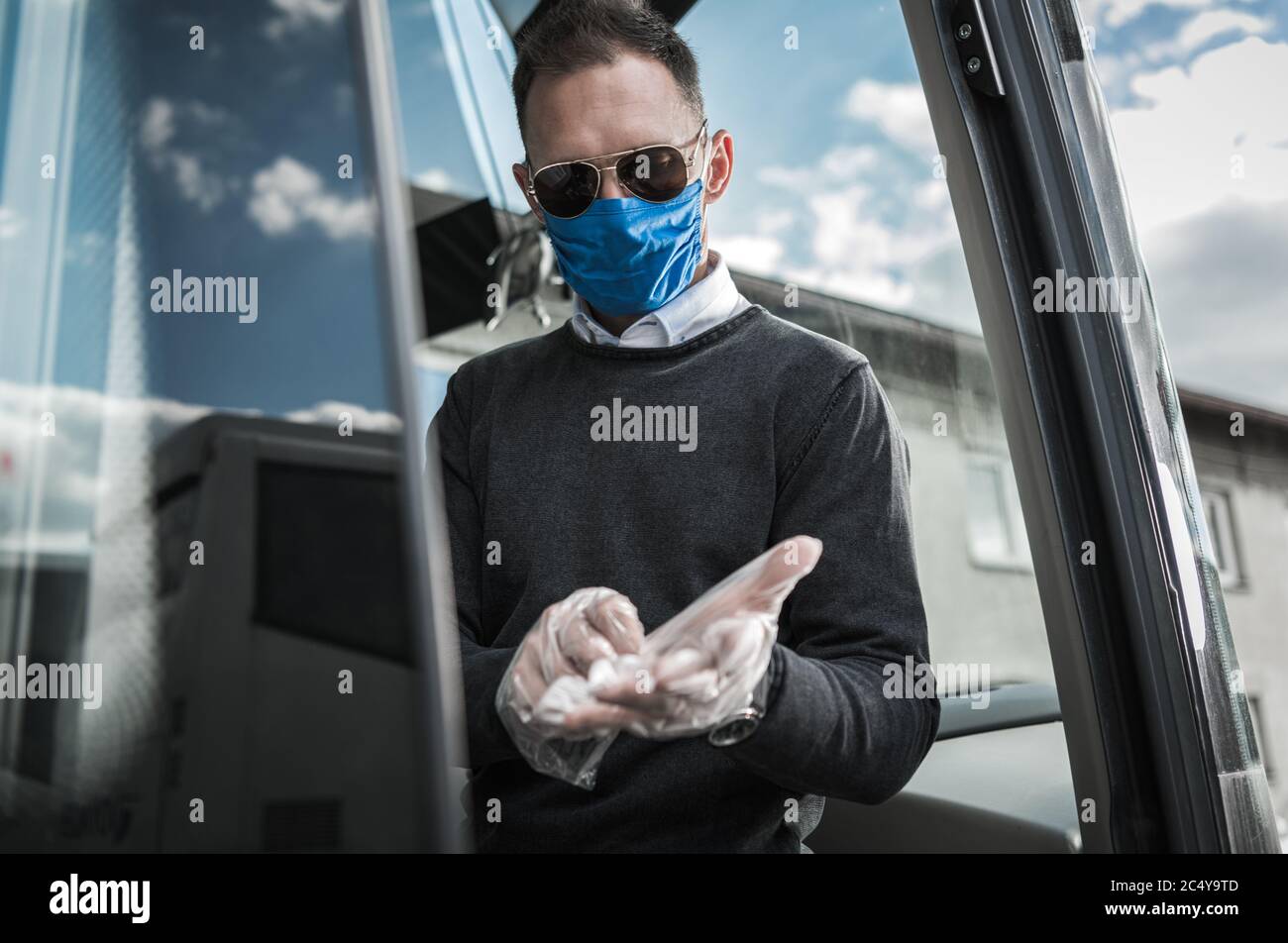 Autista autobus caucasico con maschera protettiva per il viso indossare i guanti e prepararsi al lavoro durante la pandemia. Foto Stock