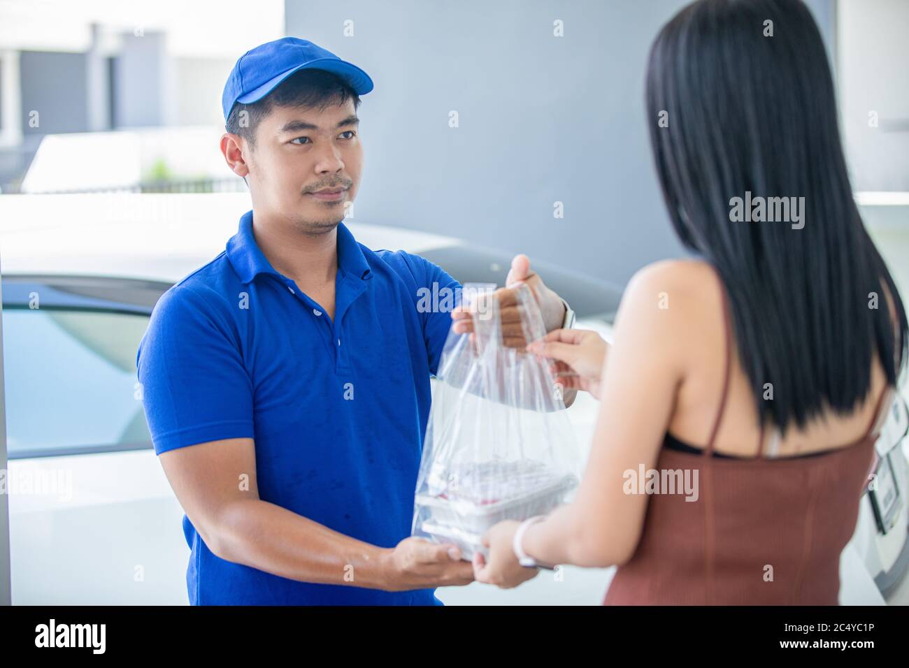 I militari asiatici che indossano una divisa blu con un cappuccio blu e maneggiano le scatole di cibo in sacchetti di plastica da dare al cliente di fronte alla casa Foto Stock