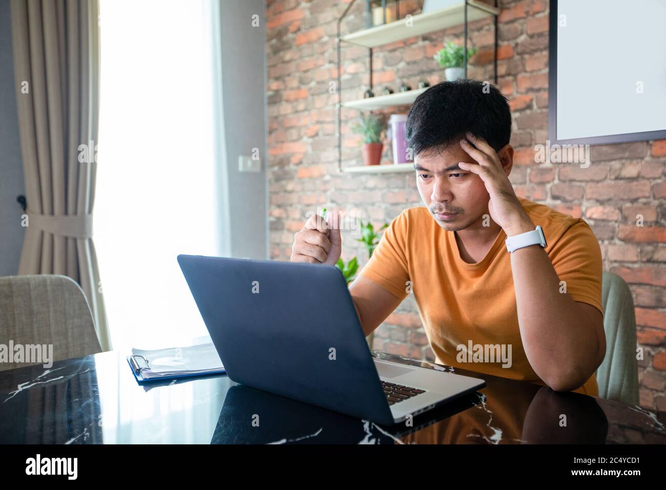 L'uomo asiatico usa un computer portatile e lavora duro e riunione a casa e lui è stressato e mal di testa. Foto Stock