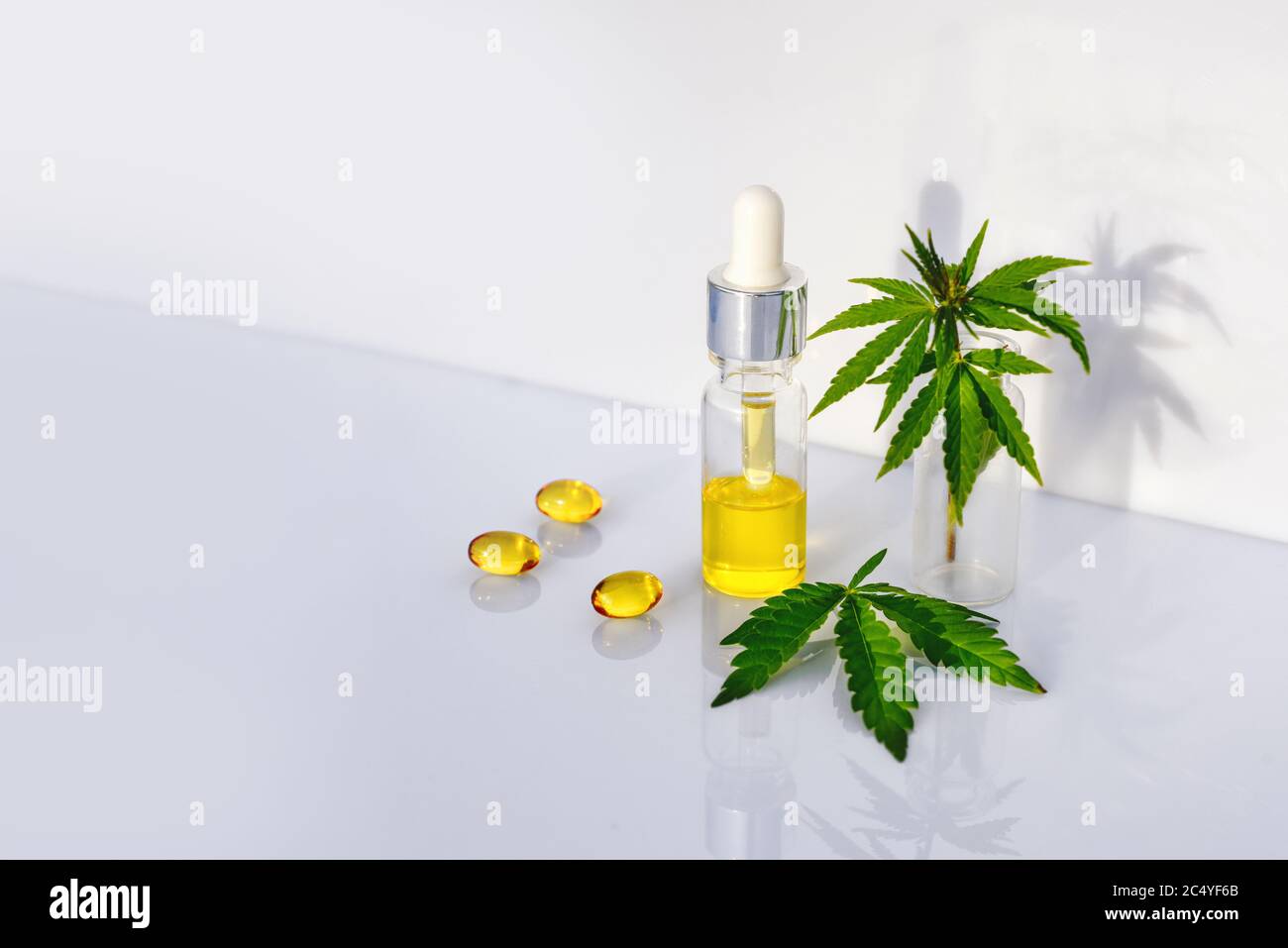 Olio CBD farmaceutico, capsule su tavola bianca da laboratorio con foglie di cannabis Foto Stock
