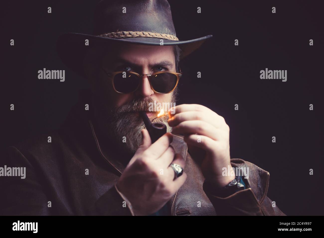 Minaccioso cowboy vintage in piedi con pipa per fumare. Studio girato su sfondo scuro Foto Stock