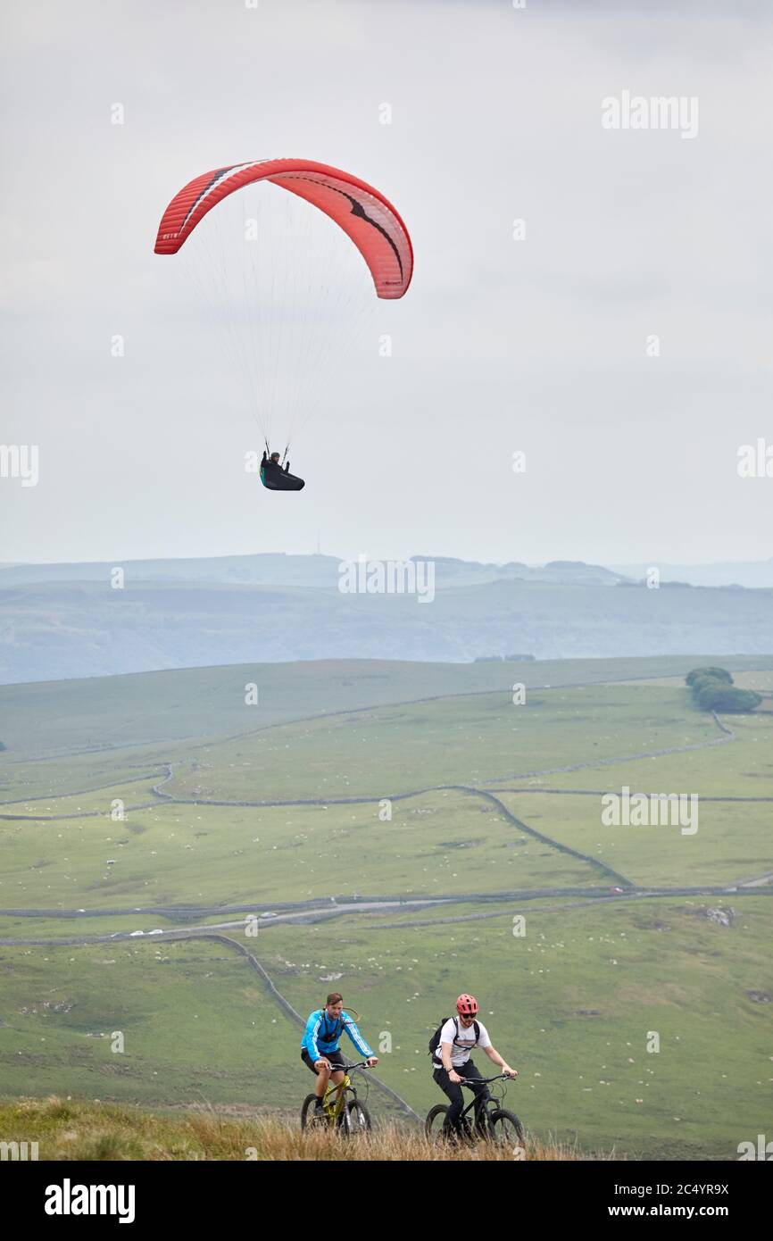 Parapendio al largo della collina di MAM Tor vicino a Castleton, nella vetta alta del Derbyshire, Inghilterra, mentre i ciclisti cavalcano lungo la cima Foto Stock