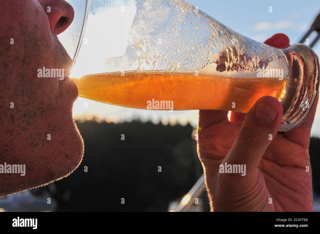 Primo piano di un uomo non rasato che beve una birra all'aperto. Retroilluminata dal sole. Persone, bevande, alcol, tempo libero, stile di vita concetto. Versione del modello Foto Stock
