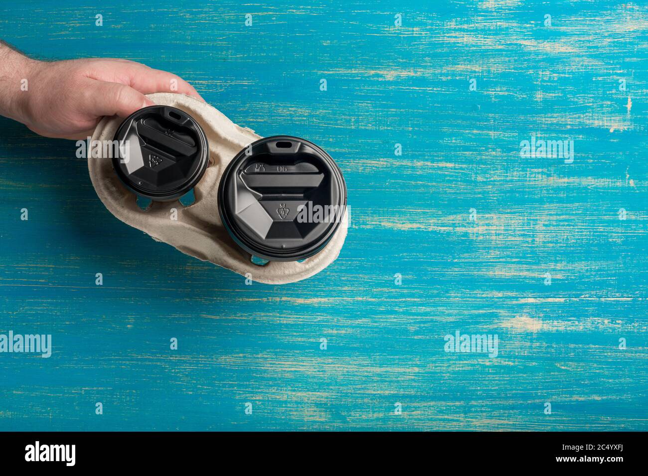 Due tazze di carta monouso di caffè e un portabicchieri in mano maschile su sfondo di legno blu. Foto Stock