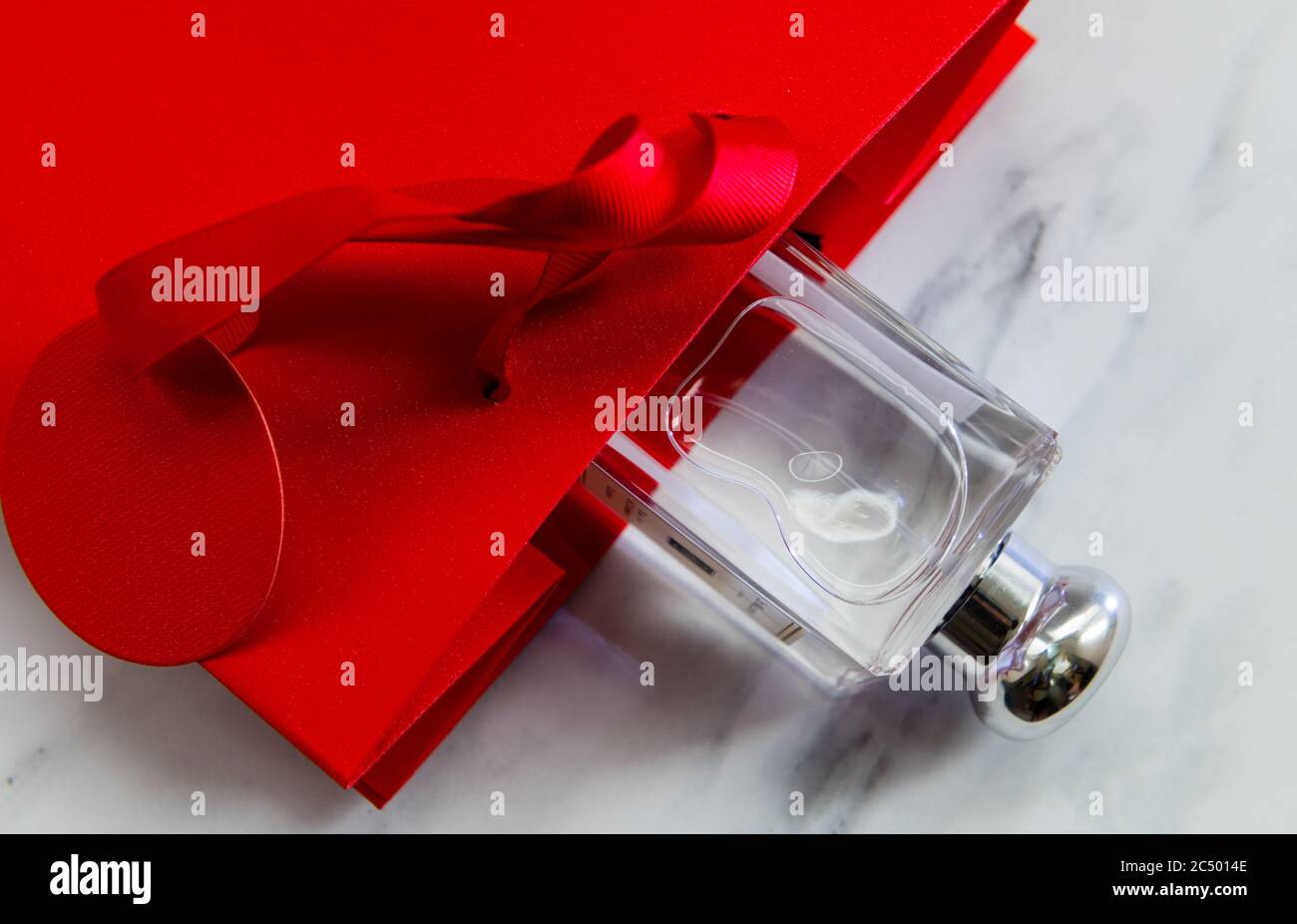 Una borsa regalo rossa con una bottiglia di profumo isolata su sfondo grigio marmo. Foto Stock