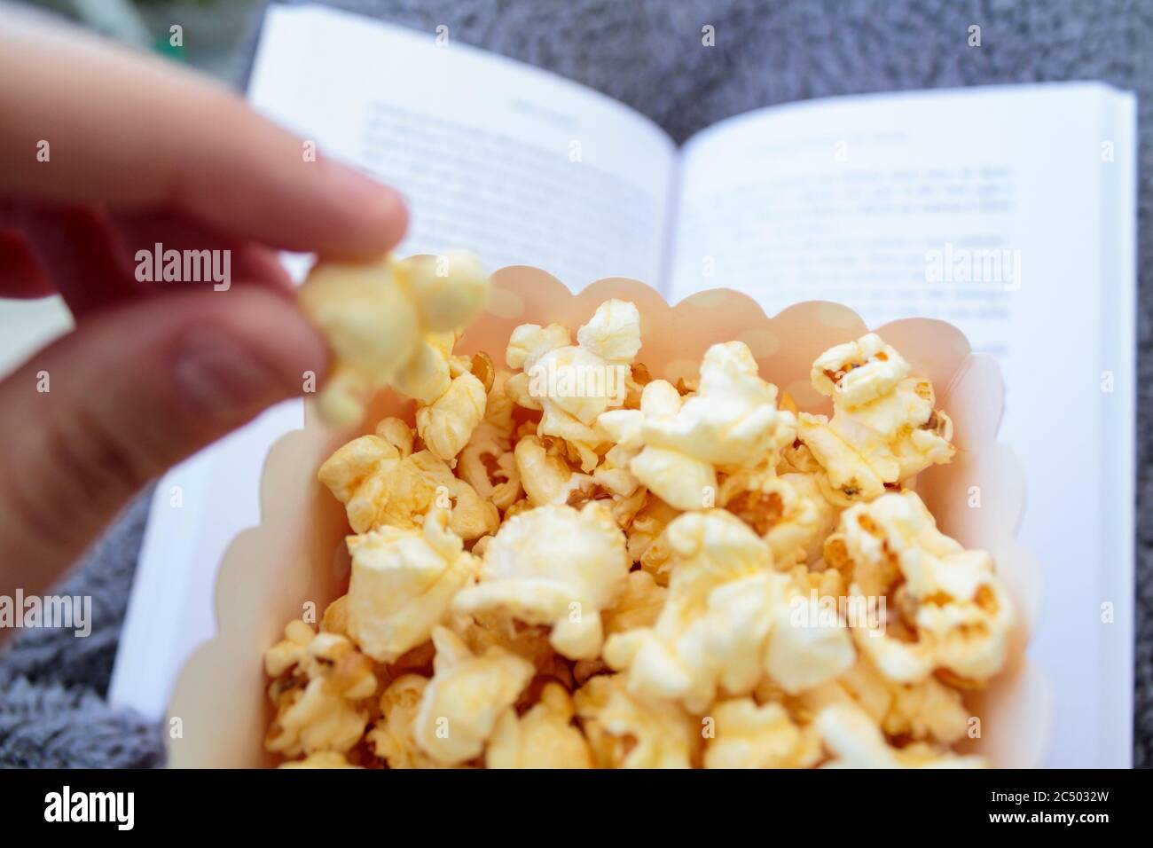 Mangiare popcorn mentre si legge un libro Foto Stock