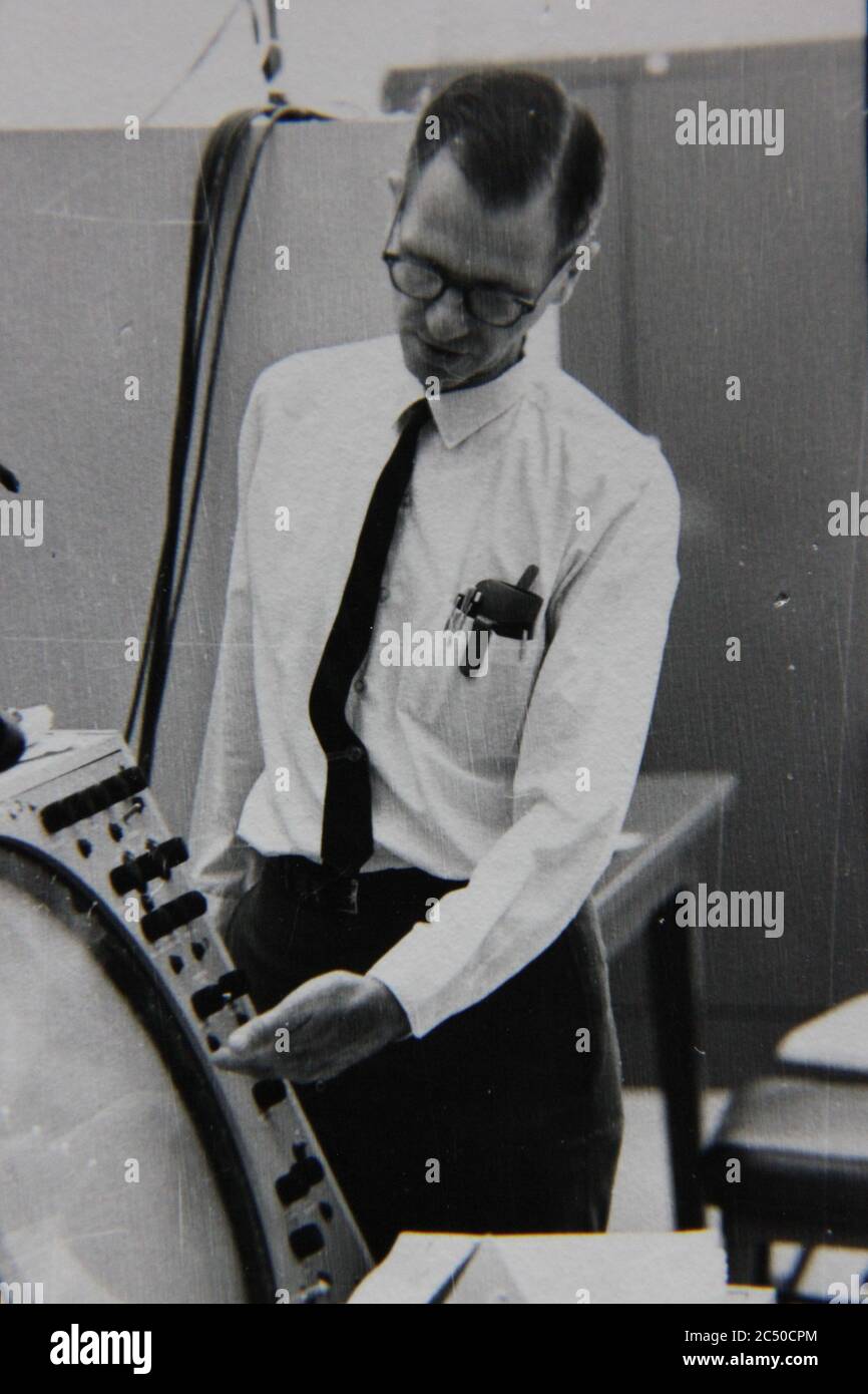 Bella fotografia in bianco e nero anni '70 di un uomo professionista che discute di un pannello di controllo del computer. Foto Stock