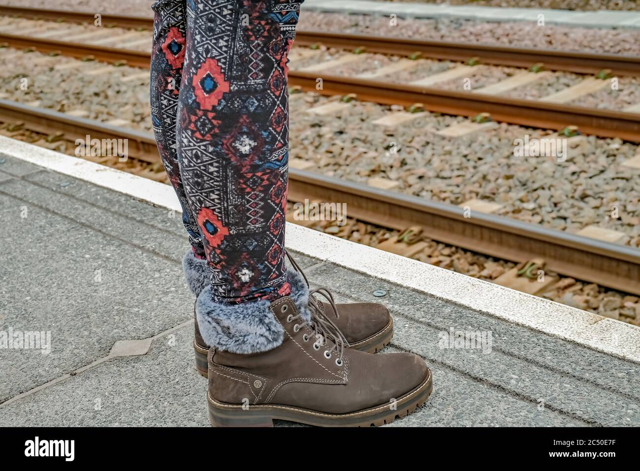 Piedi e gambe di una donna non identificabile passener ferroviario in attesa di un treno su una piattaforma di cemento Foto Stock