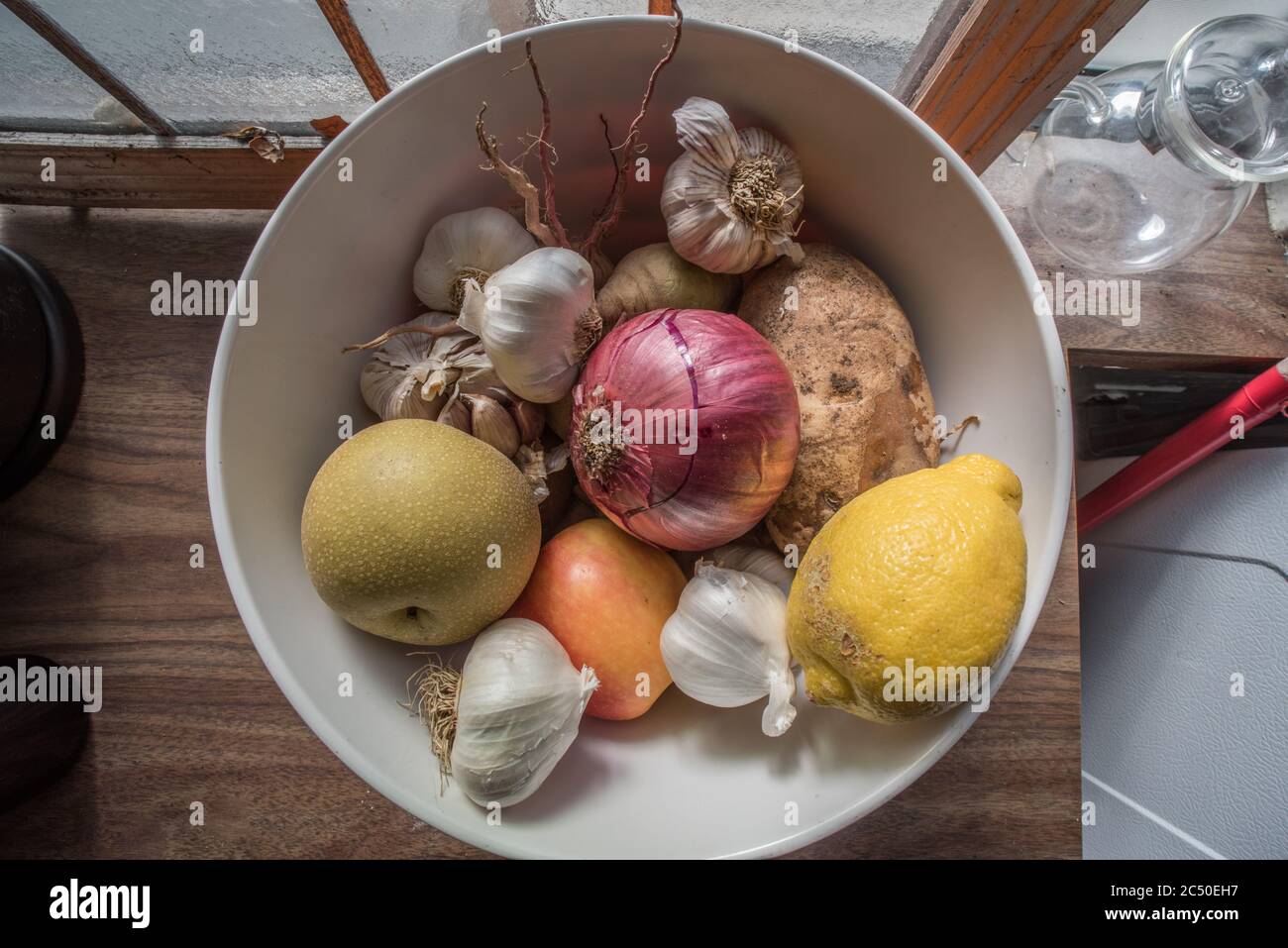 Una vita morta di una ciotola di frutta e verdura mista seduta su un piano di un bancone in una cucina. Foto Stock