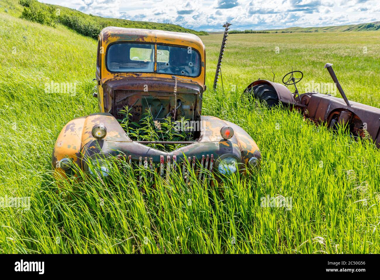 Abbandonato antico camion giallo e trattore in erba alta vicino Wymark, SK Foto Stock