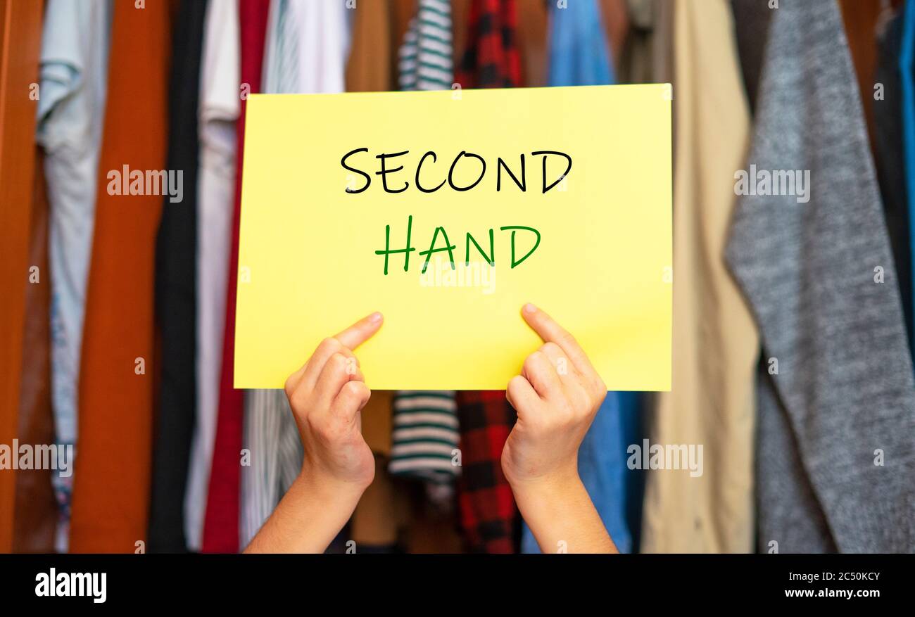 Mani che raccolgono un segno che dice la seconda mano. Abbigliamento usato. Acquista abbigliamento usato. Foto Stock