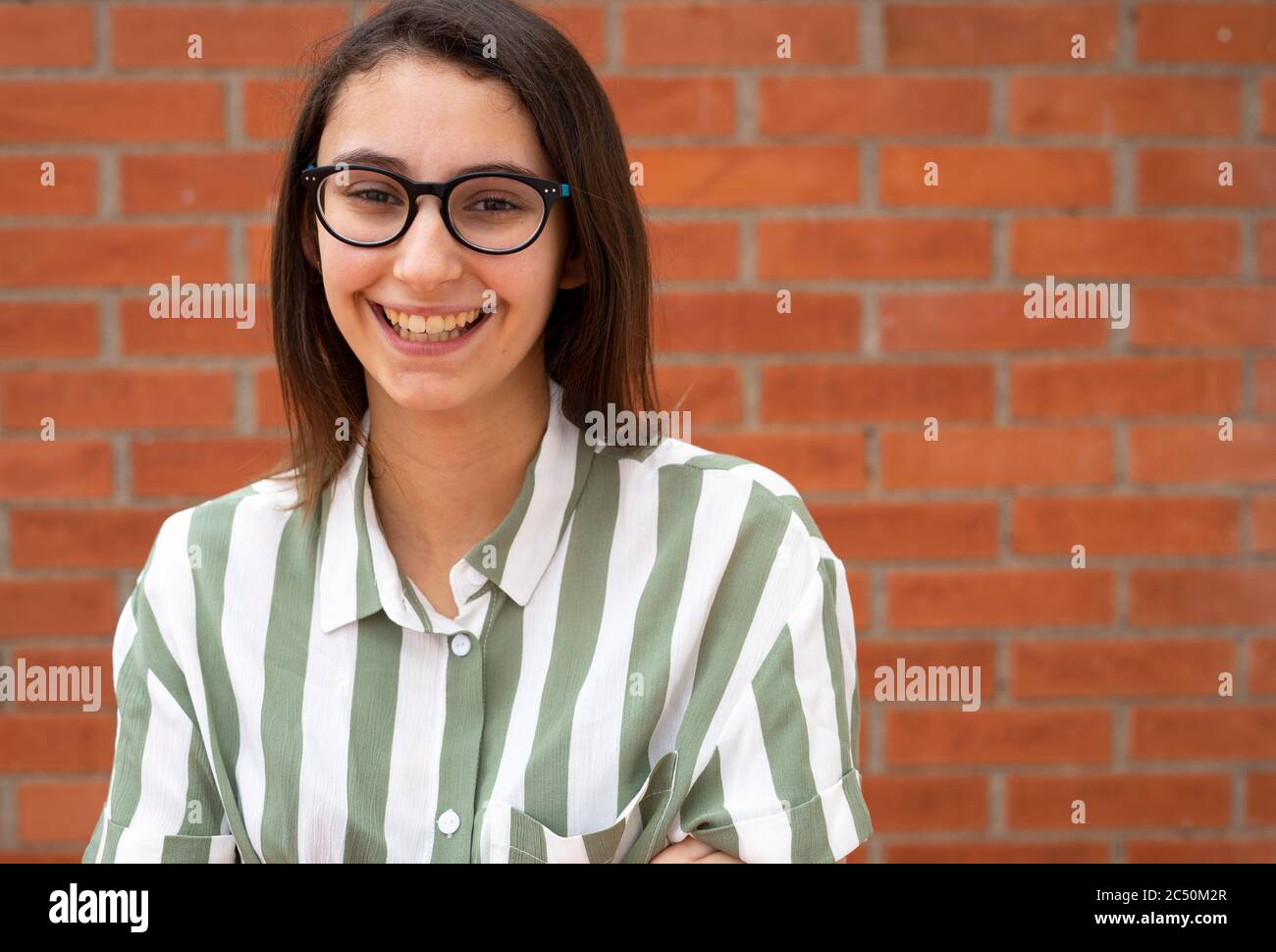 donna d'affari con occhiali e camicia a righe sorridente su un muro di mattoni. Spazio di copia per il testo. Foto Stock