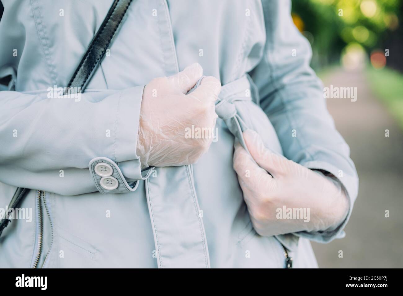 Una ragazza in guanti medici stringe la cintura di un cappotto di primavera sulla strada. Foto Stock