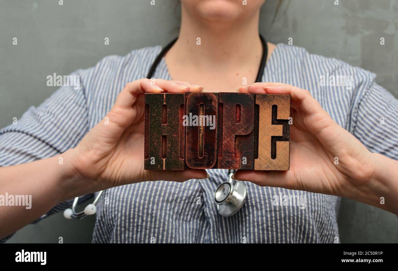 Un medico con stetoscopio contiene la parola 'speranza' fatta di lettere tipografiche in legno. Personale sanitario, infermiere, assistenza medica di alta qualità Foto Stock