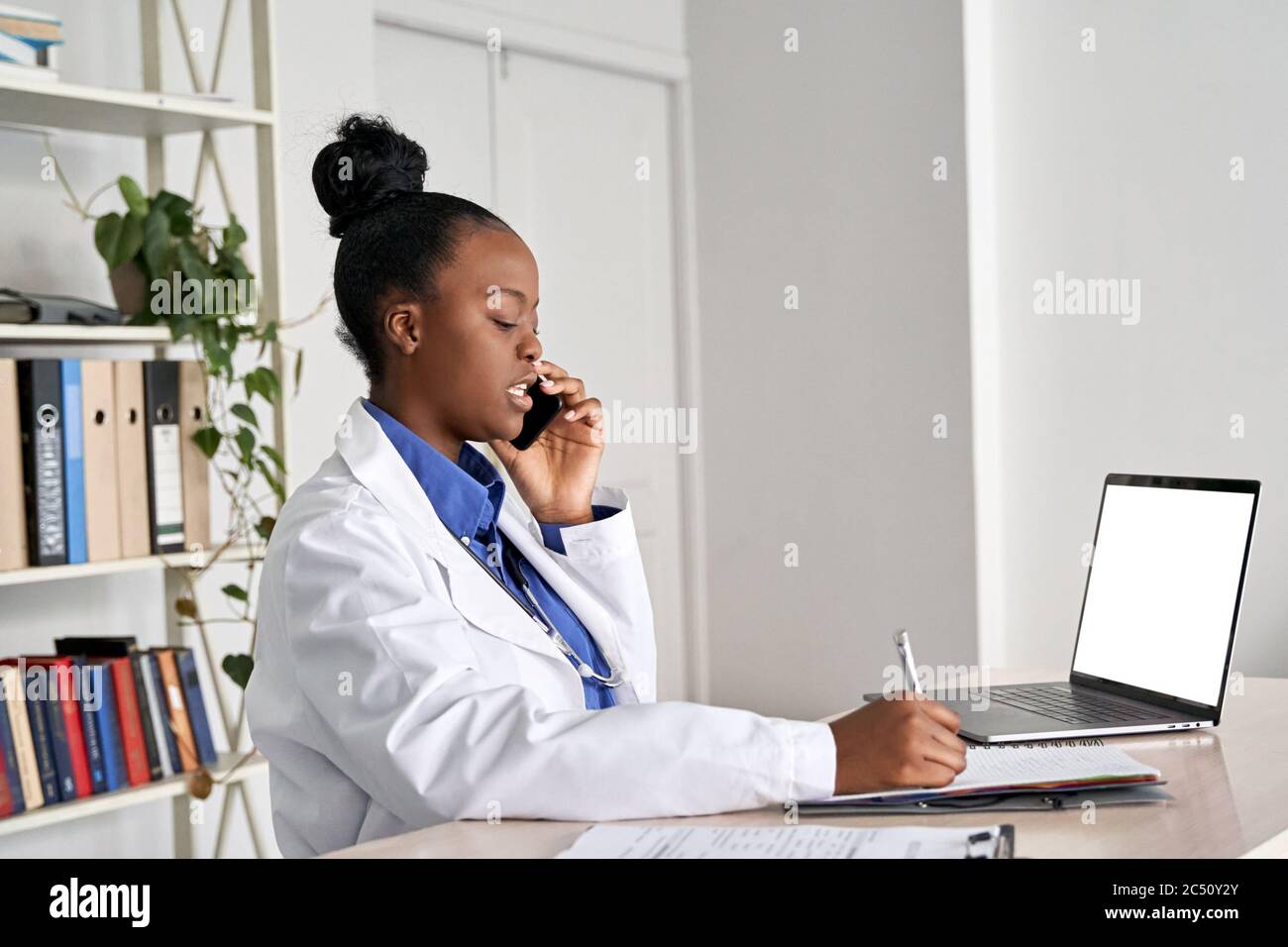 Giovane donna africana medico medico che tiene telefono che parla sul cellulare al lavoro. Foto Stock