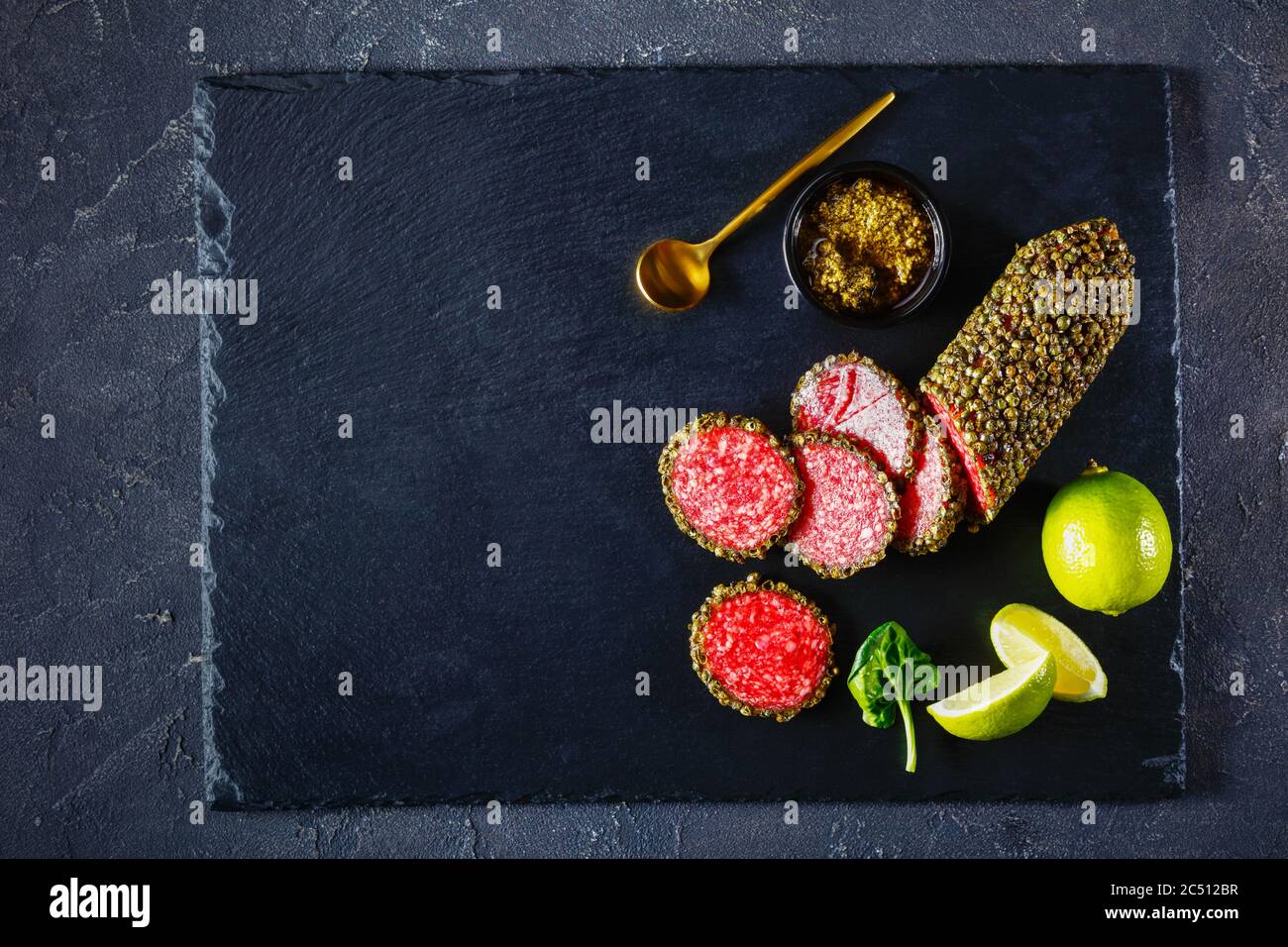 salame rivestito con pepe verde intero e hanno affettato su una tavola di pietra nera e servito con pesto al basilico e zeppe di lime, piatto, primo piano, ho Foto Stock