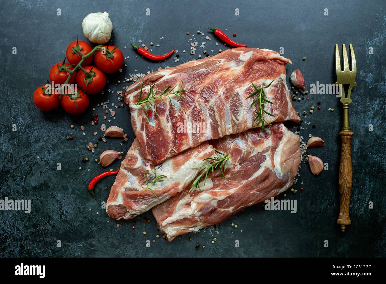 Rack di costolette di maiale crudo condite su una superficie nera Foto Stock