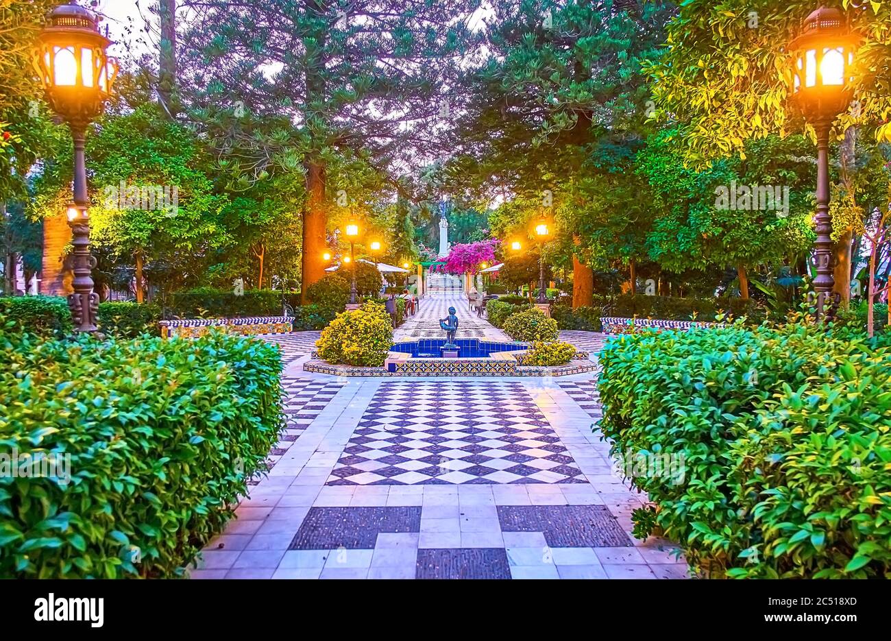 Serata nel giardino topiario Alameda Apodaca e Marques de Comillas con pavimento a scacchiera, alberi sparsi, cespugli tagliati, lanterna retrò in ghisa Foto Stock