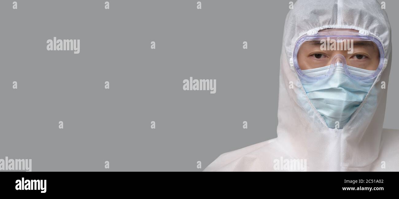 Un uomo asiatico che indossa tuta protettiva, maschere mediche e occhiali di protezione su sfondo grigio. Foto Stock