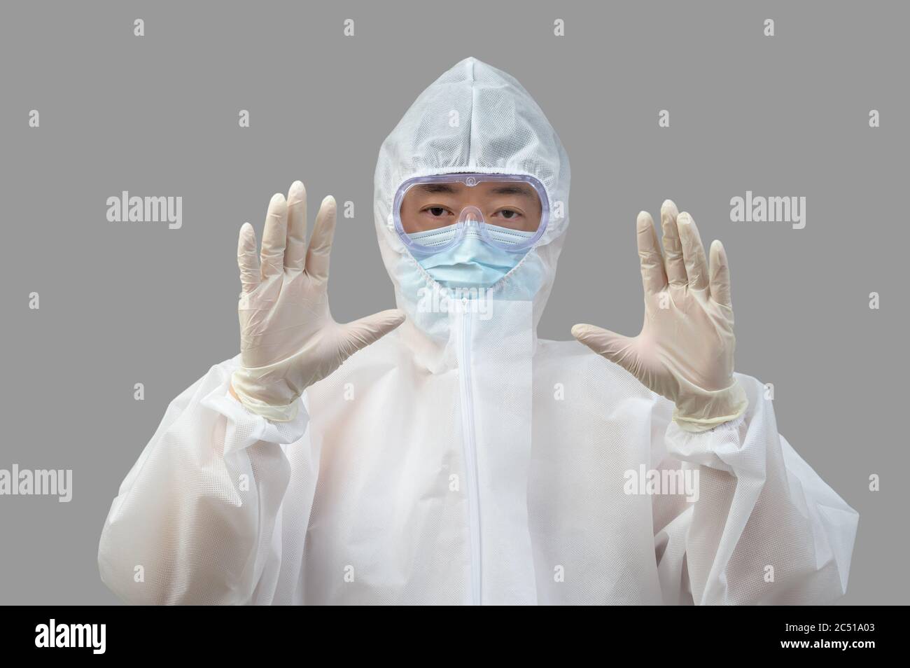 Un uomo asiatico che indossa tuta protettiva, maschere mediche e occhiali di protezione su sfondo grigio. Foto Stock