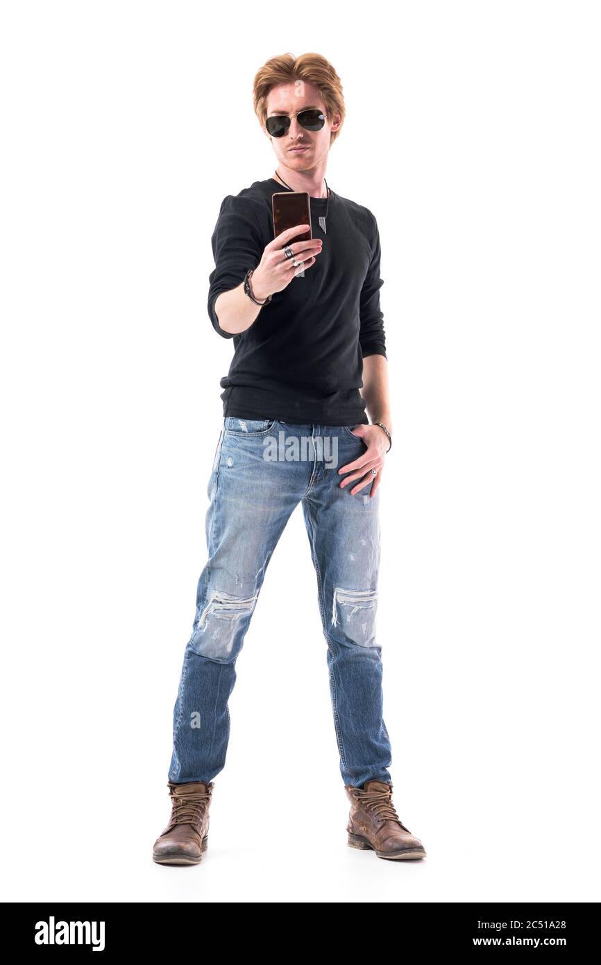 Bel giovane elegante uomo rosso in jeans che scatta foto con il cellulare. Ritratto a lunghezza intera isolato su sfondo bianco. Foto Stock