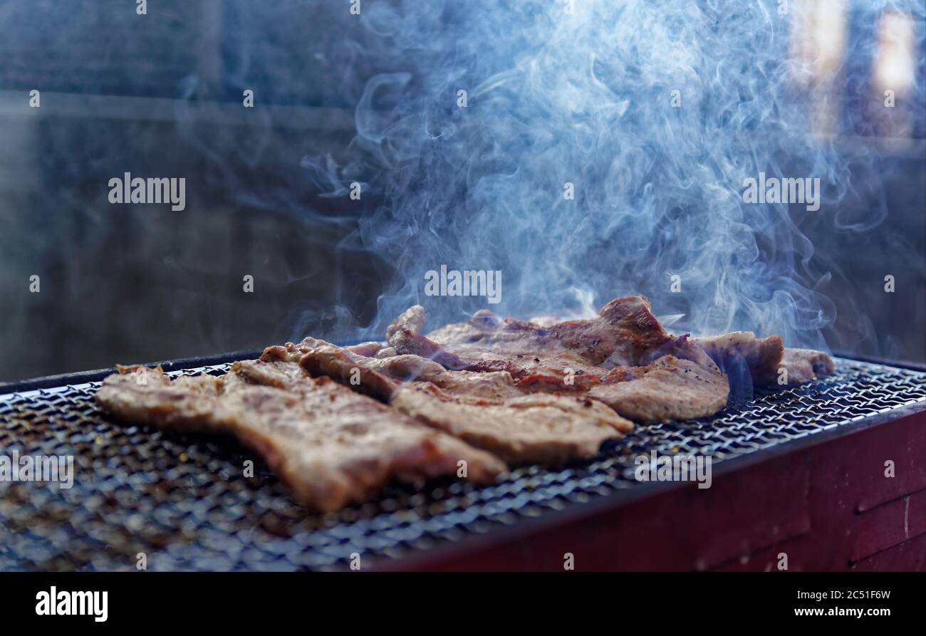 Strisce di carne che fumano su una piccola griglia all'aperto nel tardo pomeriggio Foto Stock